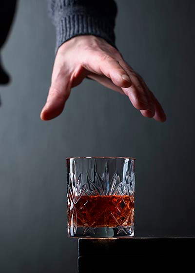 мужчина тянет руку к стакану с алкоголем